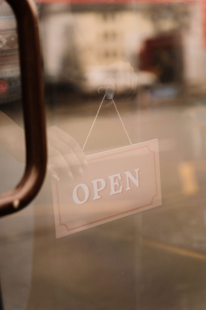 A glass door with a hanging 'OPEN' sign, reflecting an urban street scene, suggesting business availability.